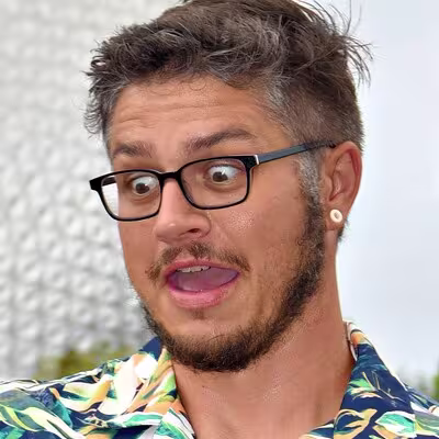 Person with glasses and short hair making a surprised expression while wearing a colorful patterned shirt.