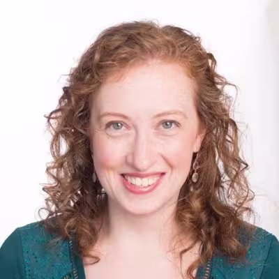 Smiling person with curly red hair against a light background.