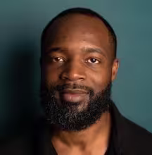Smiling man with a full beard against a dark teal background.