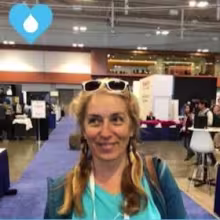 Person with braided hair and sunglasses on their head smiling at an indoor event or expo.