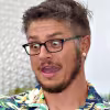 Person with glasses and short hair making a surprised expression while wearing a colorful patterned shirt.